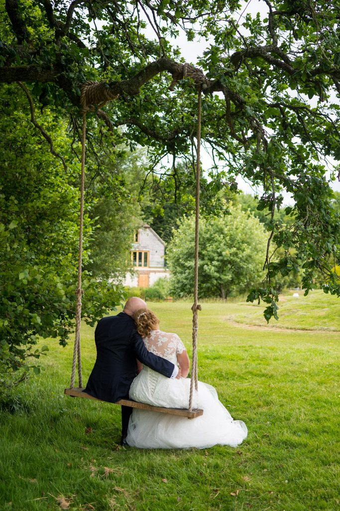 Wedding photo of a couple sitting on a tree swing looking out over a golf green at Brookfield Barn near Horsham