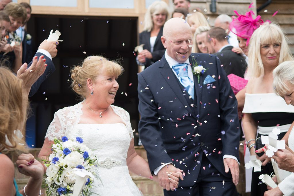 Wedding photo at Brookfield Barn with couple coming through confetti thrown by their guests
