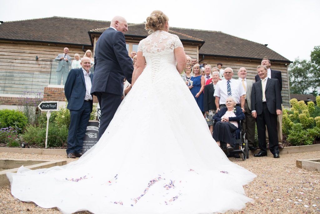 Wedding couple at Brookfield barn, photo of wedding dress detail with crowd in the background