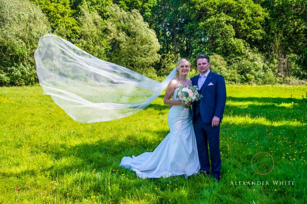 wedding photo of a bride and groom standing together with the bride's veil caught in a breeze
