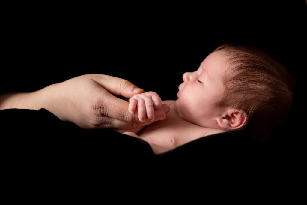 Newborn in mother's arms holding it's mother's finger