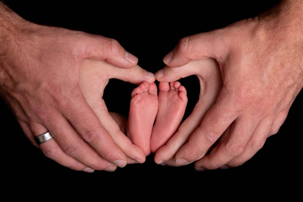 Newborn baby feet held by mother and father's hands in the shape of a heart