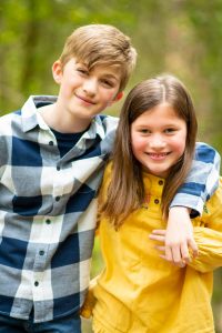Siblings hugging and smiling at the camera on an outdoor family photo shoot