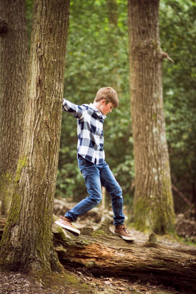 A boy walking along a tree trunk in the woods