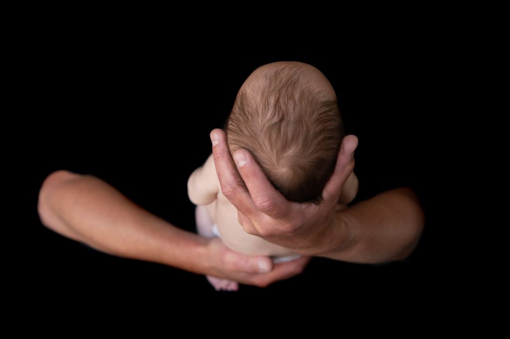 Newborn baby held in father's arms on a black background