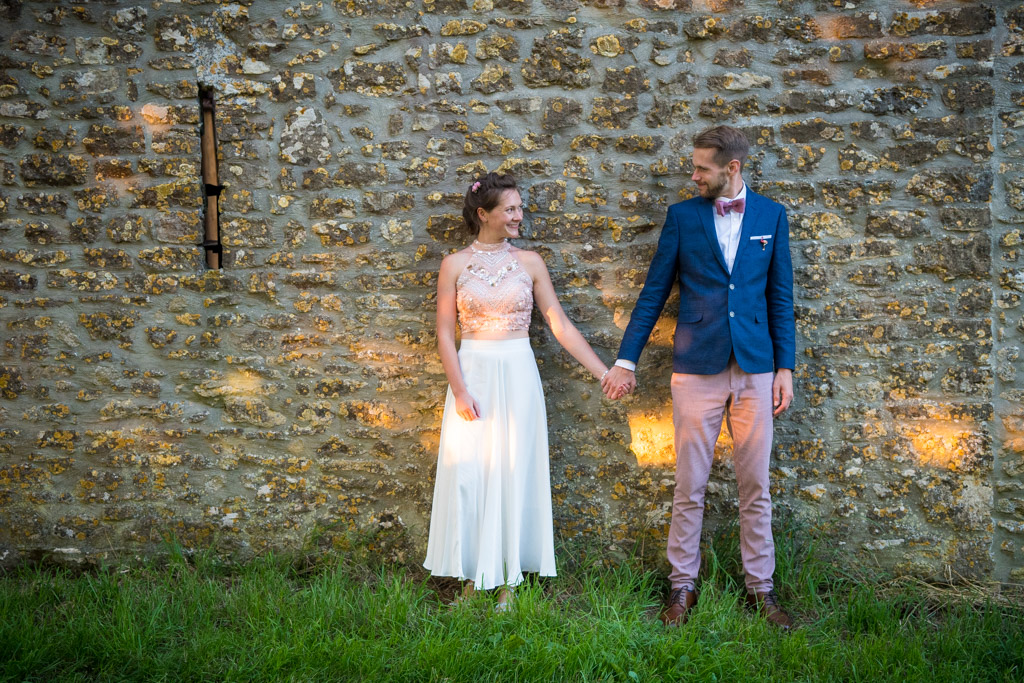 Bride and groom standing in front of a stone wall holding hands