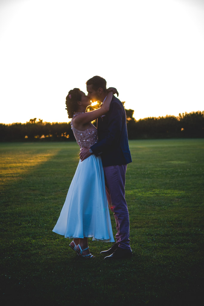 Bride and groom kissing with the sun behind them