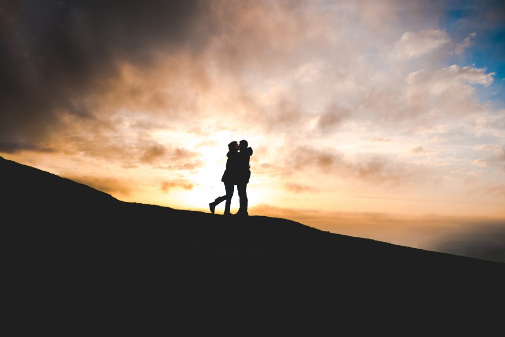 A couple sharing a kiss, having just got engaged in front of a sunset in Sussex