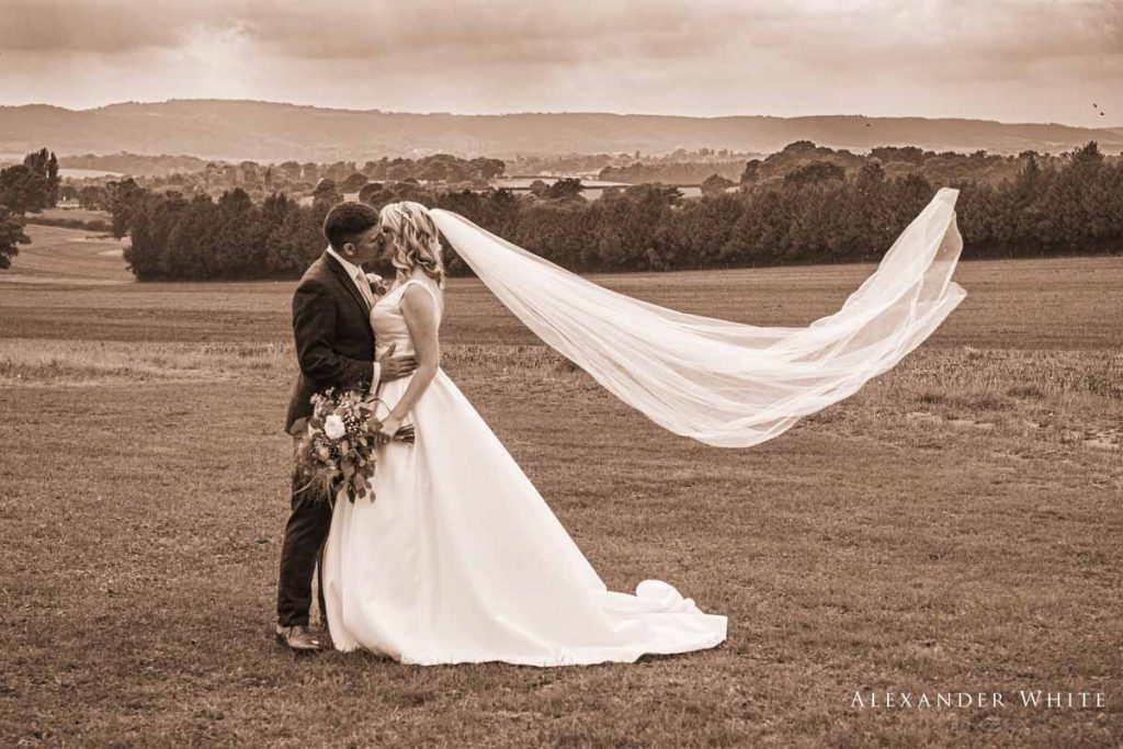 Bride and Groom kissing in front of the view from Fitzleroi Barn