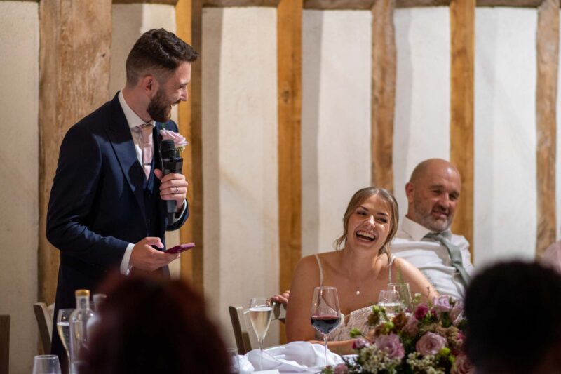 Groom giving his speech with the bride laughing at a joke