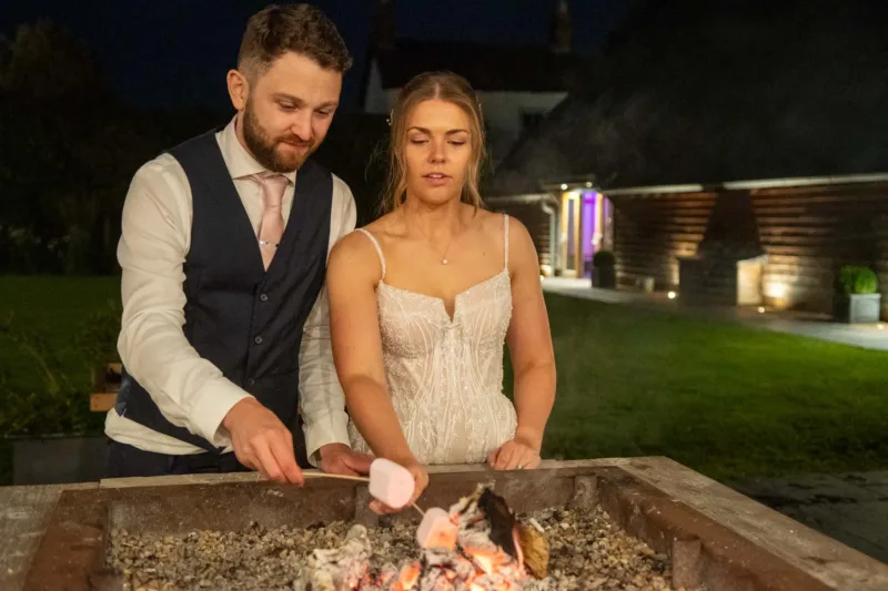 Bride and groom toasting marshmallows over a fire pit