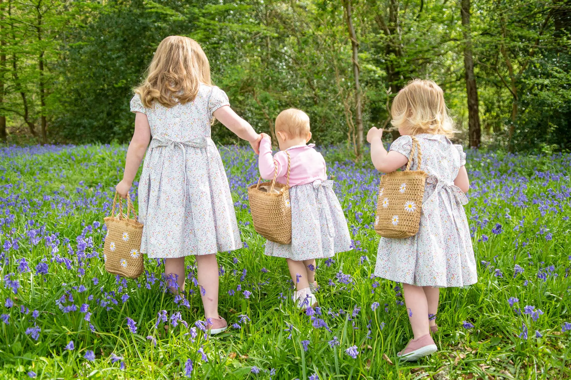 A family photograph of three young girls walking in a bluebell woodland